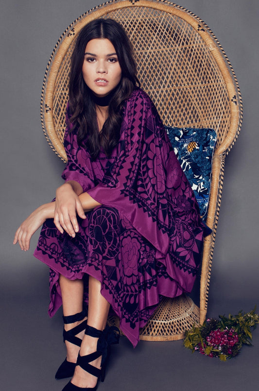 “Model wearing a Holland Street printed silk kaftan with floral motifs, sitting on a wicker chair.”