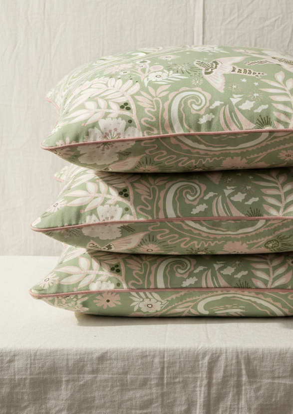 A stack of hand‑drawn Holland Street “Park Life” pattern printed cushions, featuring birds, boats, and flowers in pale green, pink and moss green tones, designed in Britain.