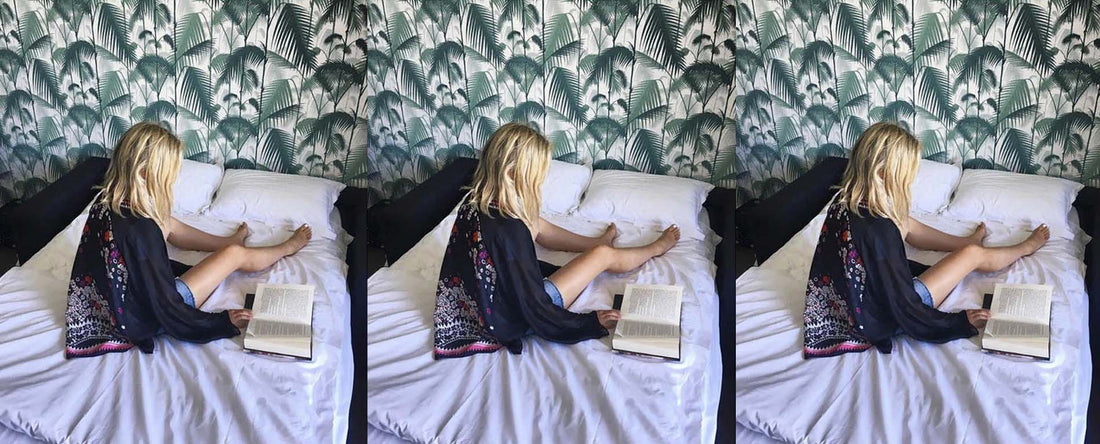 woman wearing kimono robe reading book. tropical wallpaper behind.  